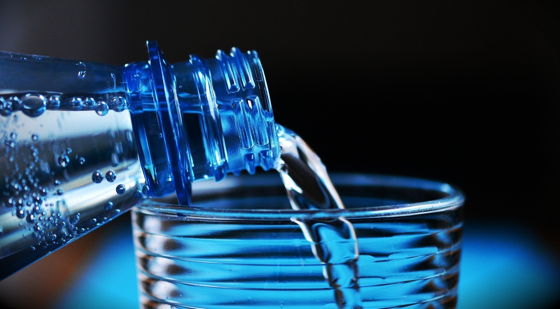 A water bottle being emptied into a glass with a blue-black background out of focus